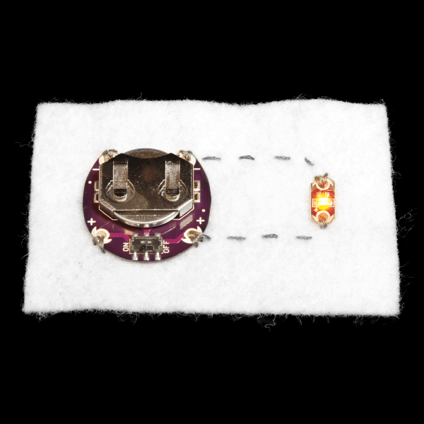 Placa LilyPad Battery Board cosida con hilo conductor a una placa LilyPad LED encendida sobre tela